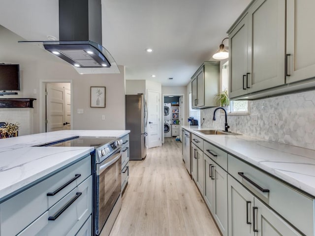 kitchen featuring tasteful backsplash, stainless steel appliances, island exhaust hood, a sink, and washer / clothes dryer