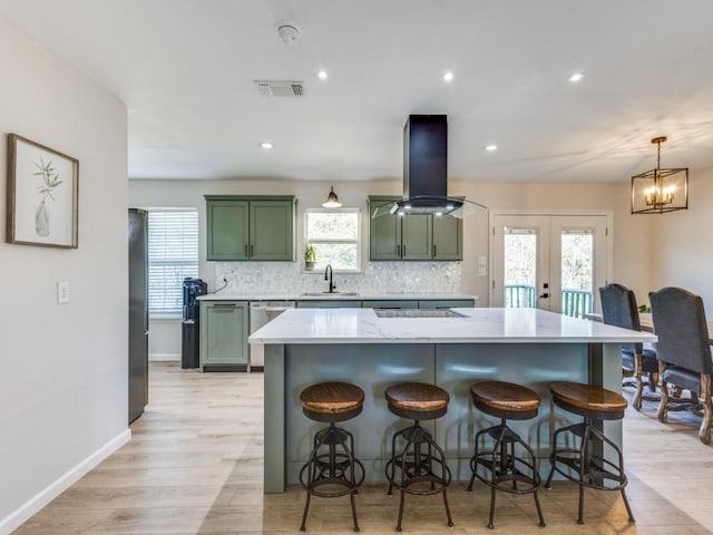 kitchen with green cabinets, visible vents, island exhaust hood, tasteful backsplash, and a sink