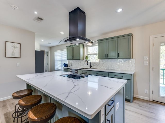 kitchen featuring island exhaust hood, green cabinetry, black electric cooktop, and backsplash