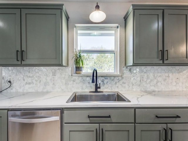 kitchen with gray cabinetry, decorative backsplash, stainless steel dishwasher, a sink, and light stone counters
