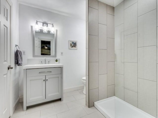 bathroom featuring tile patterned floors, tiled shower, toilet, vanity, and baseboards