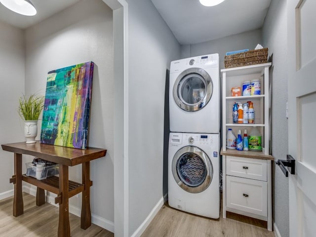 clothes washing area featuring baseboards, light wood-type flooring, stacked washer and clothes dryer, and laundry area