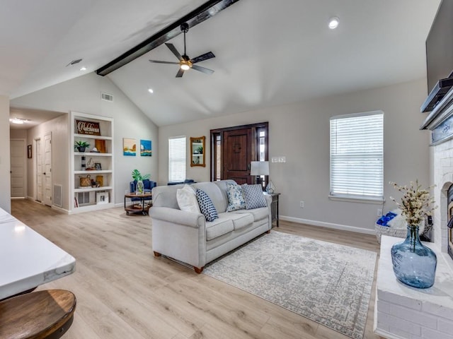 living room featuring light wood-type flooring, lofted ceiling with beams, baseboards, ceiling fan, and a brick fireplace