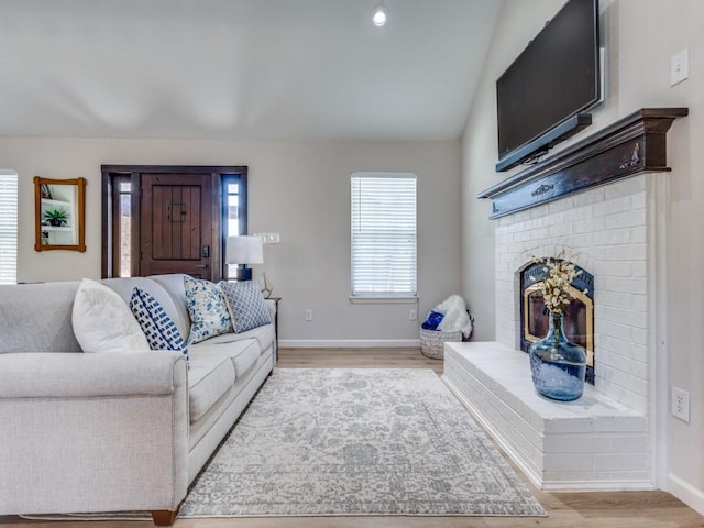 living area with light wood finished floors, baseboards, a fireplace, and vaulted ceiling