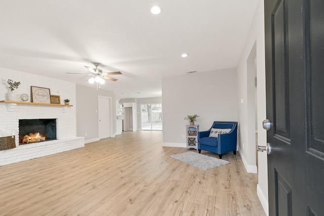 entryway with light wood finished floors, visible vents, a brick fireplace, baseboards, and ceiling fan