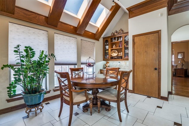 dining area featuring vaulted ceiling with skylight, arched walkways, and baseboards