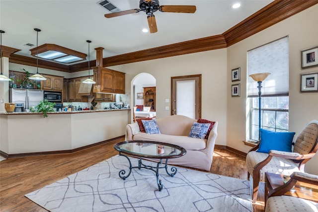 living room with arched walkways, light wood-style floors, visible vents, and crown molding