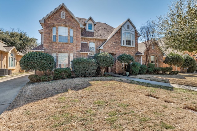 view of front of house featuring a shingled roof, a front yard, brick siding, and central air condition unit