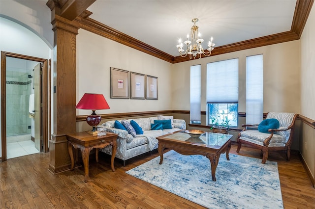 living room featuring ornate columns, ornamental molding, wood finished floors, and an inviting chandelier