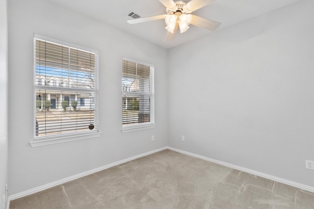 spare room with light carpet, ceiling fan, visible vents, and baseboards