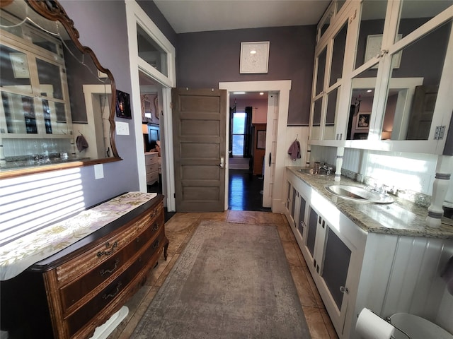 kitchen with light stone countertops, glass insert cabinets, backsplash, and a sink