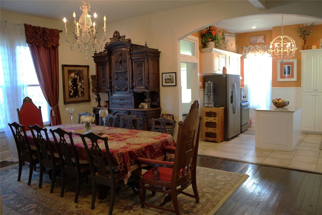 dining space with arched walkways, a healthy amount of sunlight, a notable chandelier, and light wood finished floors