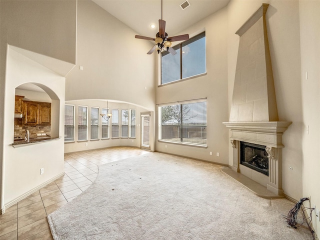 unfurnished living room with light tile patterned floors, baseboards, a ceiling fan, light colored carpet, and a fireplace