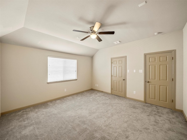 unfurnished bedroom featuring lofted ceiling, light colored carpet, visible vents, a ceiling fan, and baseboards