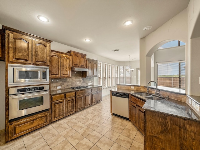 kitchen with light tile patterned flooring, under cabinet range hood, stainless steel appliances, a sink, and backsplash