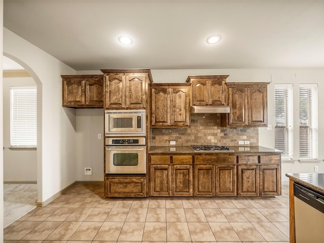 kitchen featuring under cabinet range hood, light tile patterned floors, stainless steel appliances, and decorative backsplash