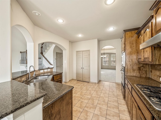 kitchen with tasteful backsplash, arched walkways, brown cabinetry, appliances with stainless steel finishes, and a sink