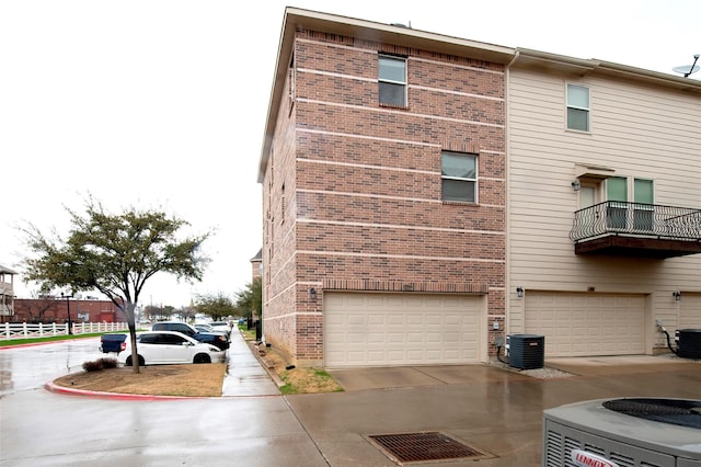 view of side of property featuring a garage, driveway, brick siding, and central air condition unit