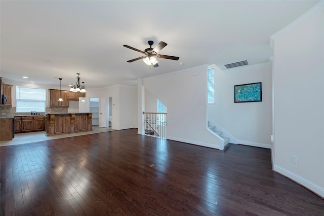 unfurnished living room with dark wood-style flooring, visible vents, ornamental molding, baseboards, and ceiling fan with notable chandelier