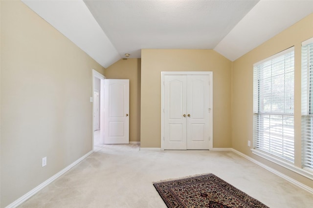 unfurnished bedroom with baseboards, vaulted ceiling, a closet, and light colored carpet