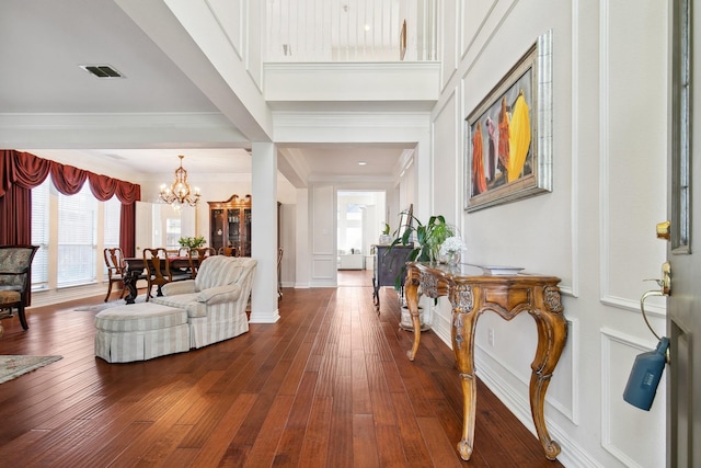 foyer entrance featuring dark wood-style floors, visible vents, a high ceiling, ornamental molding, and a chandelier