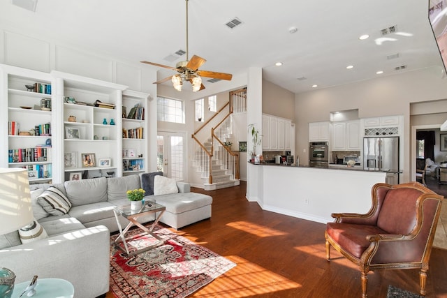 living area with visible vents, a towering ceiling, a ceiling fan, stairway, and dark wood finished floors