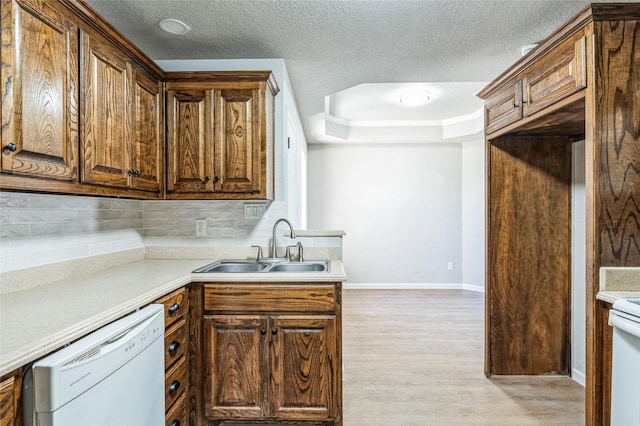 kitchen featuring light wood finished floors, decorative backsplash, a sink, dishwasher, and baseboards