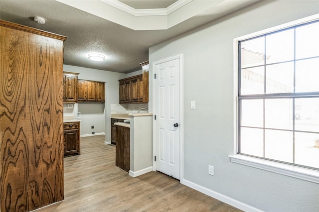 kitchen featuring a textured ceiling, baseboards, light wood-style floors, light countertops, and crown molding