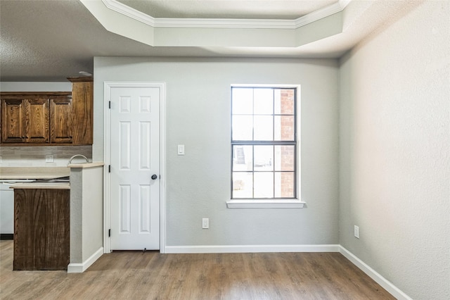 kitchen with crown molding, a raised ceiling, light wood-style flooring, and baseboards