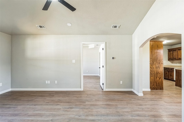 unfurnished room with light wood-style flooring, visible vents, arched walkways, and a ceiling fan