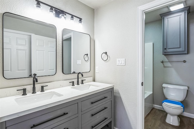 bathroom featuring double vanity, wood finished floors, a sink, and toilet