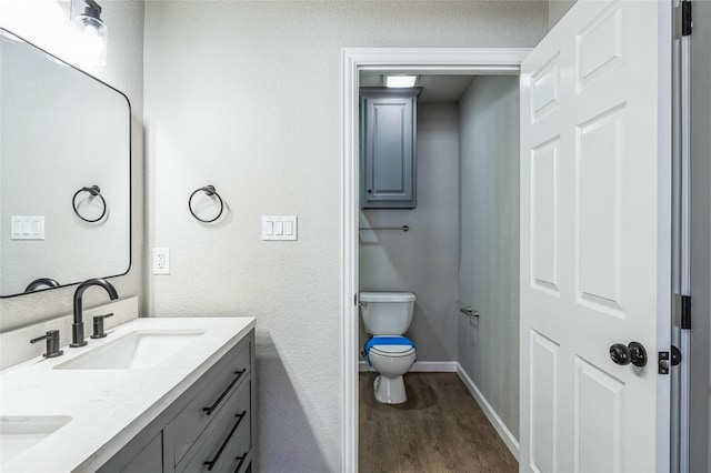 bathroom featuring double vanity, toilet, a sink, wood finished floors, and baseboards