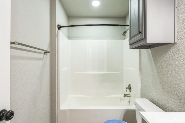 bathroom with toilet, shower / tub combination, vanity, and a textured wall