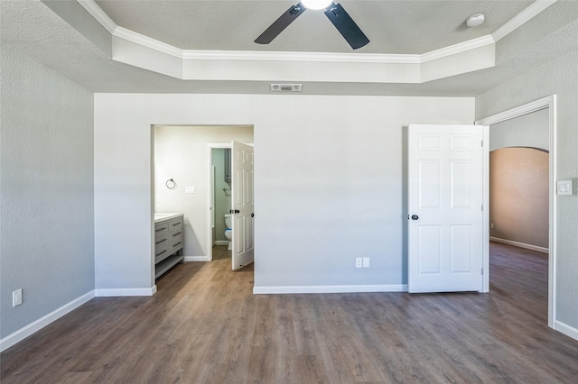 unfurnished bedroom with visible vents, arched walkways, a tray ceiling, and wood finished floors