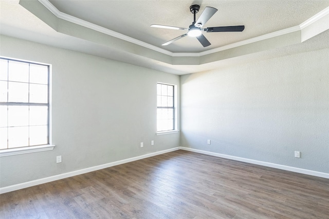 empty room featuring a raised ceiling, ornamental molding, wood finished floors, and baseboards