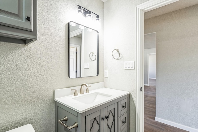 bathroom featuring baseboards, a textured wall, toilet, wood finished floors, and vanity