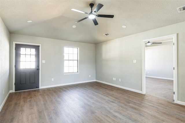 foyer with lofted ceiling, a textured ceiling, wood finished floors, and visible vents