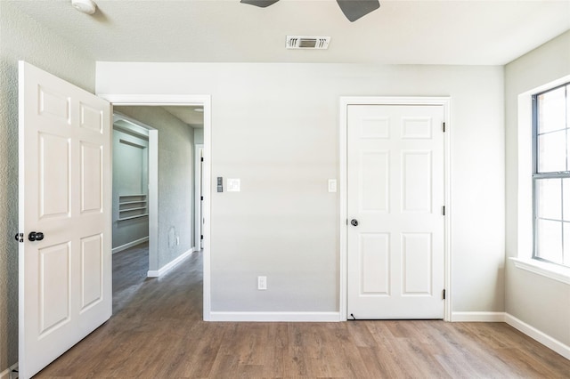 unfurnished bedroom featuring a ceiling fan, visible vents, baseboards, and wood finished floors