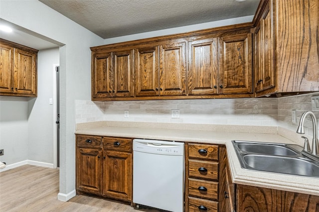 kitchen featuring tasteful backsplash, light countertops, white dishwasher, a sink, and light wood-type flooring