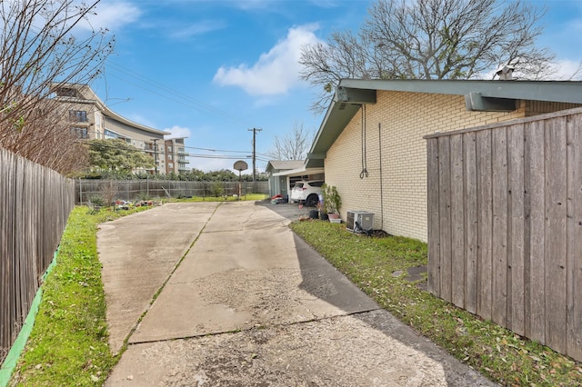 view of side of home featuring driveway, brick siding, fence, and central air condition unit