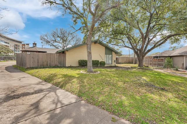 view of property exterior featuring brick siding, fence, and a lawn