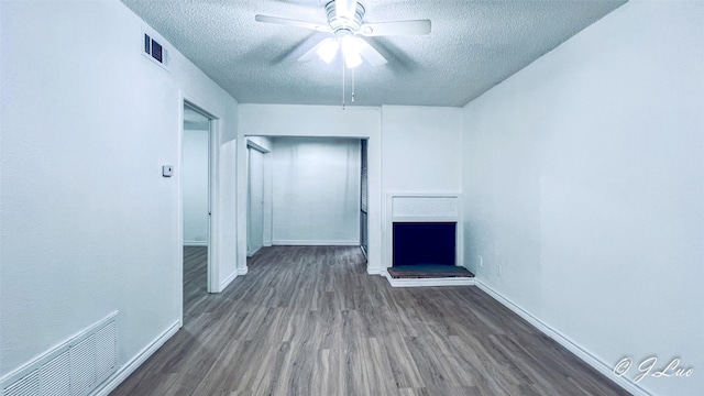 unfurnished living room with visible vents, a fireplace with raised hearth, a textured ceiling, and wood finished floors