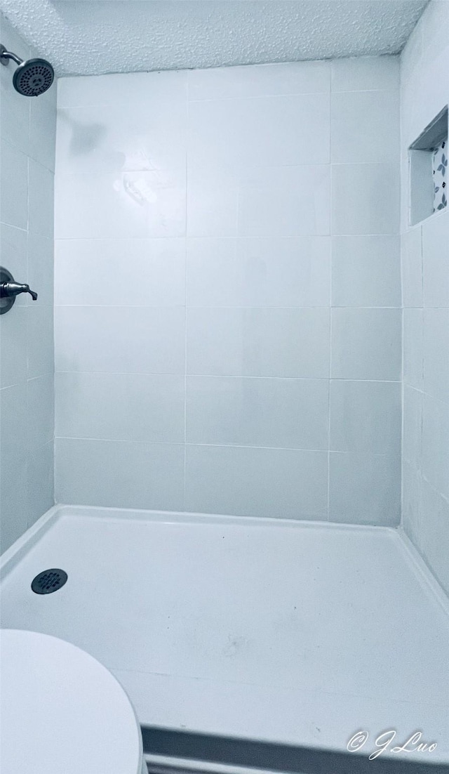 full bath with tiled shower, a textured ceiling, and toilet