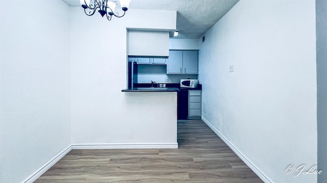 kitchen featuring baseboards, dark countertops, white microwave, wood finished floors, and a textured ceiling