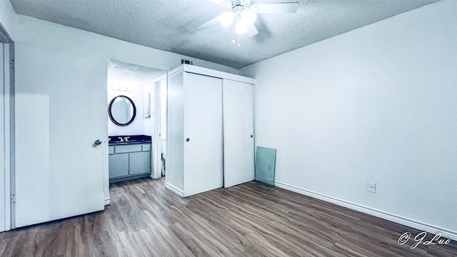 unfurnished bedroom with a closet, a sink, a textured ceiling, wood finished floors, and baseboards