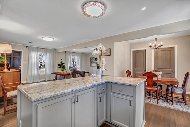 kitchen with light stone counters, open floor plan, wood finished floors, and gray cabinetry