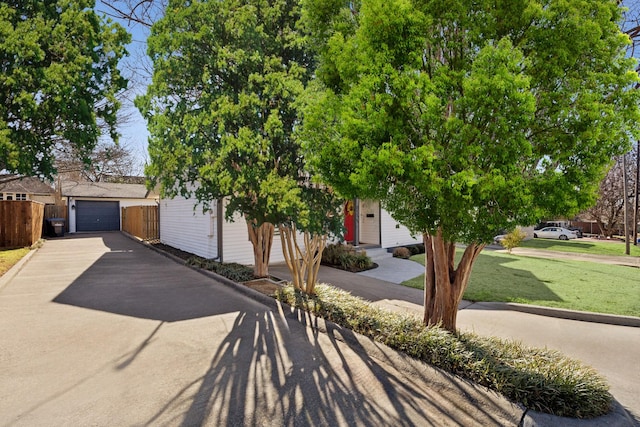 view of property hidden behind natural elements with a garage, fence, and a front yard