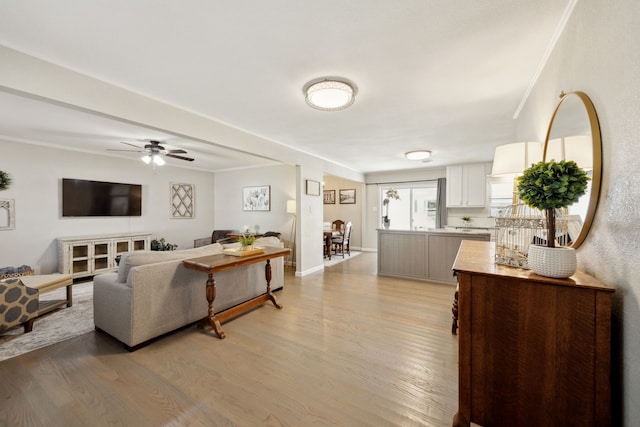 living area featuring ornamental molding, light wood finished floors, a ceiling fan, and baseboards