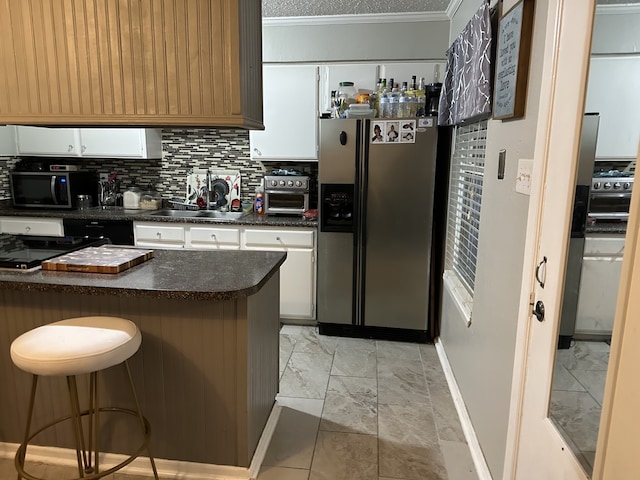 kitchen featuring stainless steel appliances, dark countertops, a sink, and white cabinetry