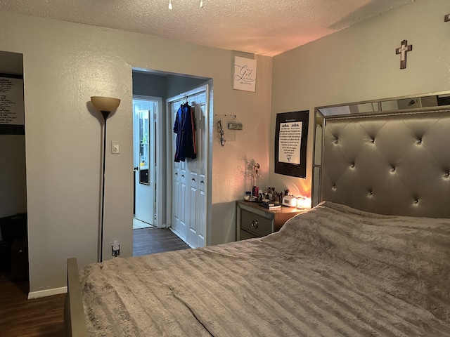 bedroom featuring a closet, dark wood-style flooring, a textured wall, and a textured ceiling